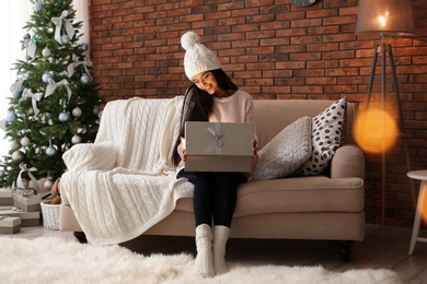 Beautiful young woman in hat opening gift box at home. Christmas celebration