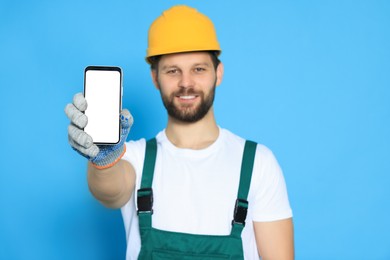 Photo of Professional repairman in uniform showing smartphone against light blue background, focus on screen