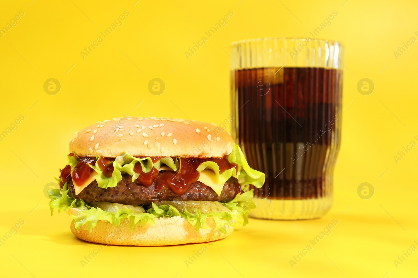 Photo of Burger with delicious patty and soda drink on yellow background