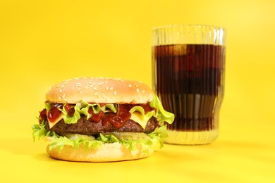 Burger with delicious patty and soda drink on yellow background