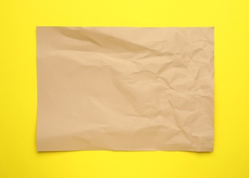 Photo of Sheet of crumpled brown paper on yellow background, top view