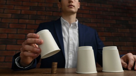 Photo of Shell game. Man showing coins under cup at wooden table, low angle view