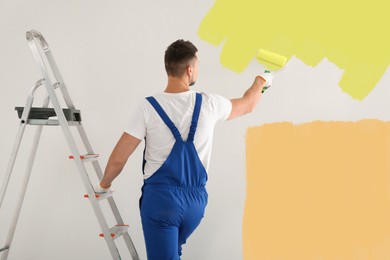 Image of Man painting wall with yellow dye indoors, back view