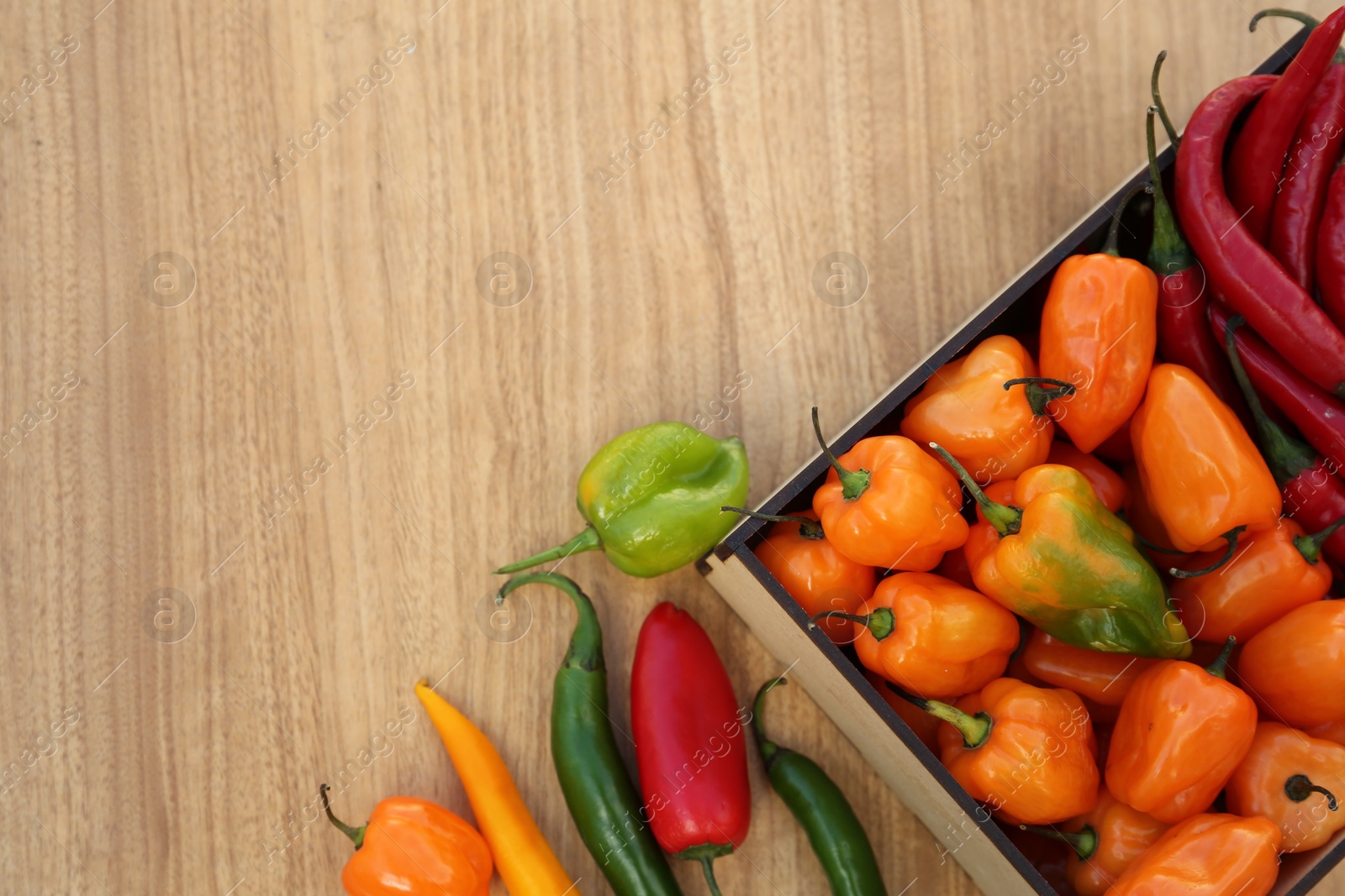 Photo of Many different fresh chilli peppers on wooden table, flat lay. Space for text