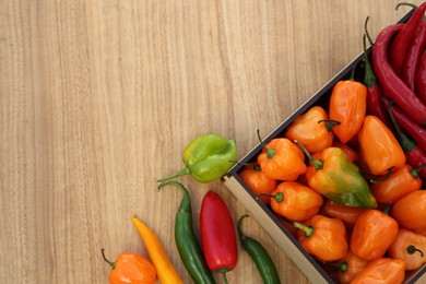Photo of Many different fresh chilli peppers on wooden table, flat lay. Space for text