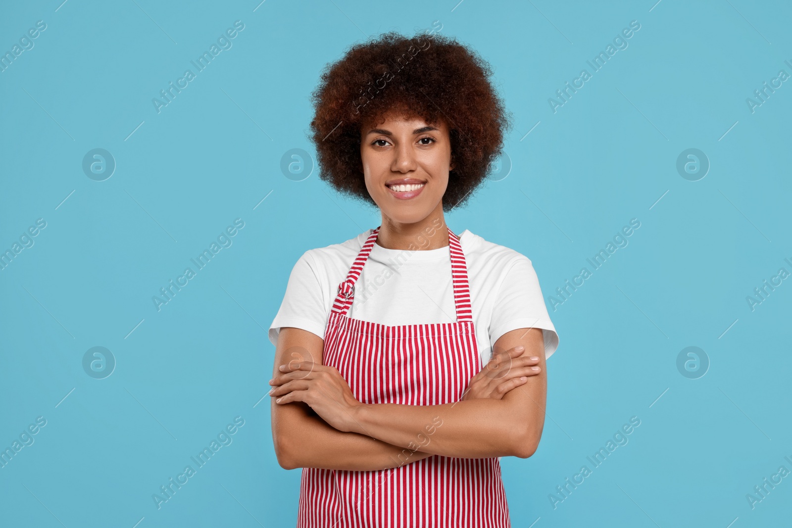 Photo of Portrait of happy young woman in apron on light blue background