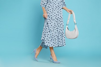 Woman with stylish bag on light blue background, closeup