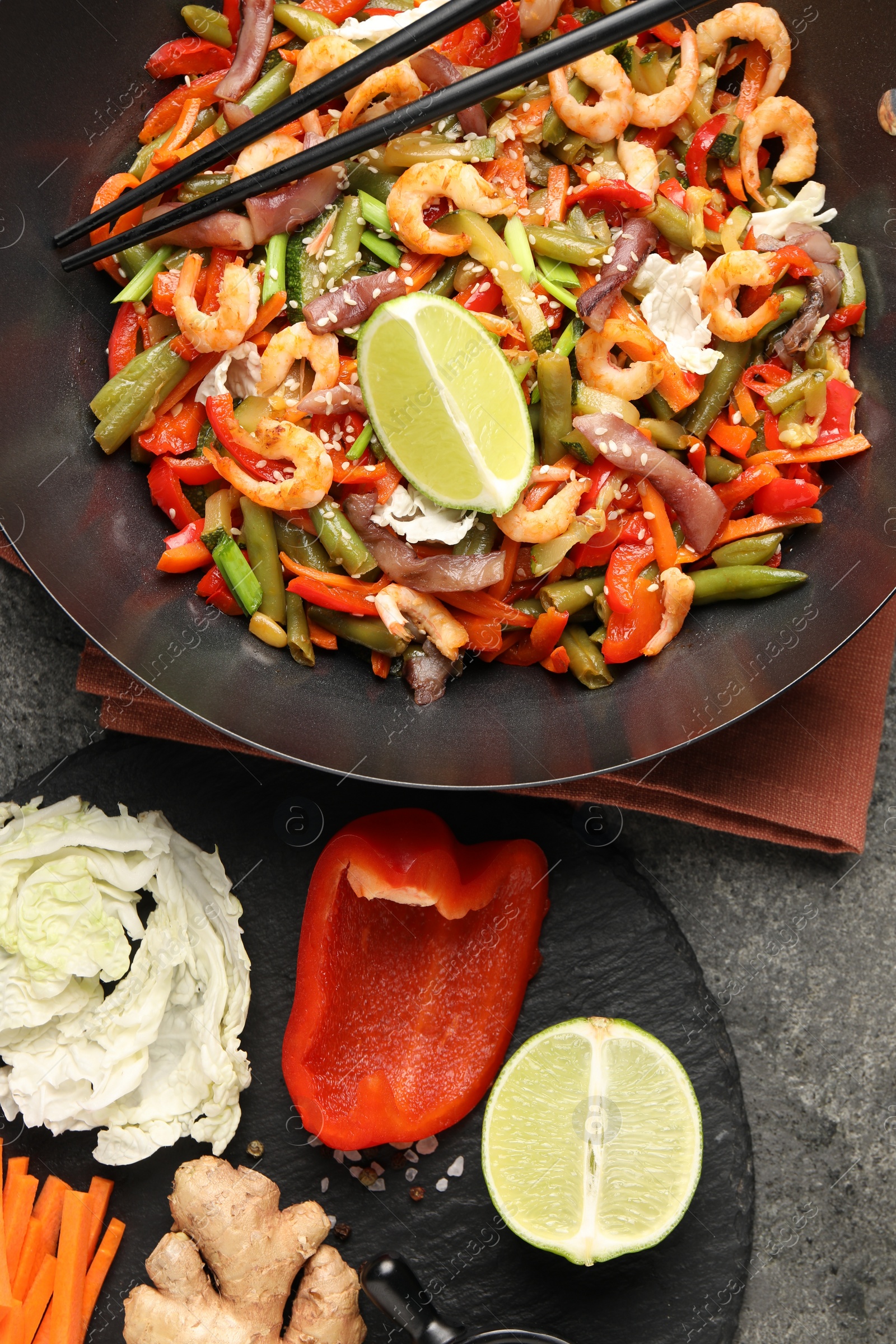 Photo of Shrimp stir fry with vegetables in wok and chopsticks on grey table, flat lay