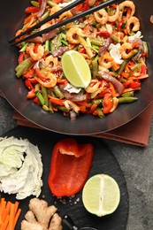 Shrimp stir fry with vegetables in wok and chopsticks on grey table, flat lay