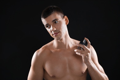 Handsome young man using perfume on black background