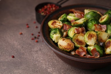 Photo of Delicious roasted Brussels sprouts and bacon in bowl on brown table, closeup. Space for text