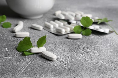 Photo of Pills and fresh green celandine on light grey table, closeup
