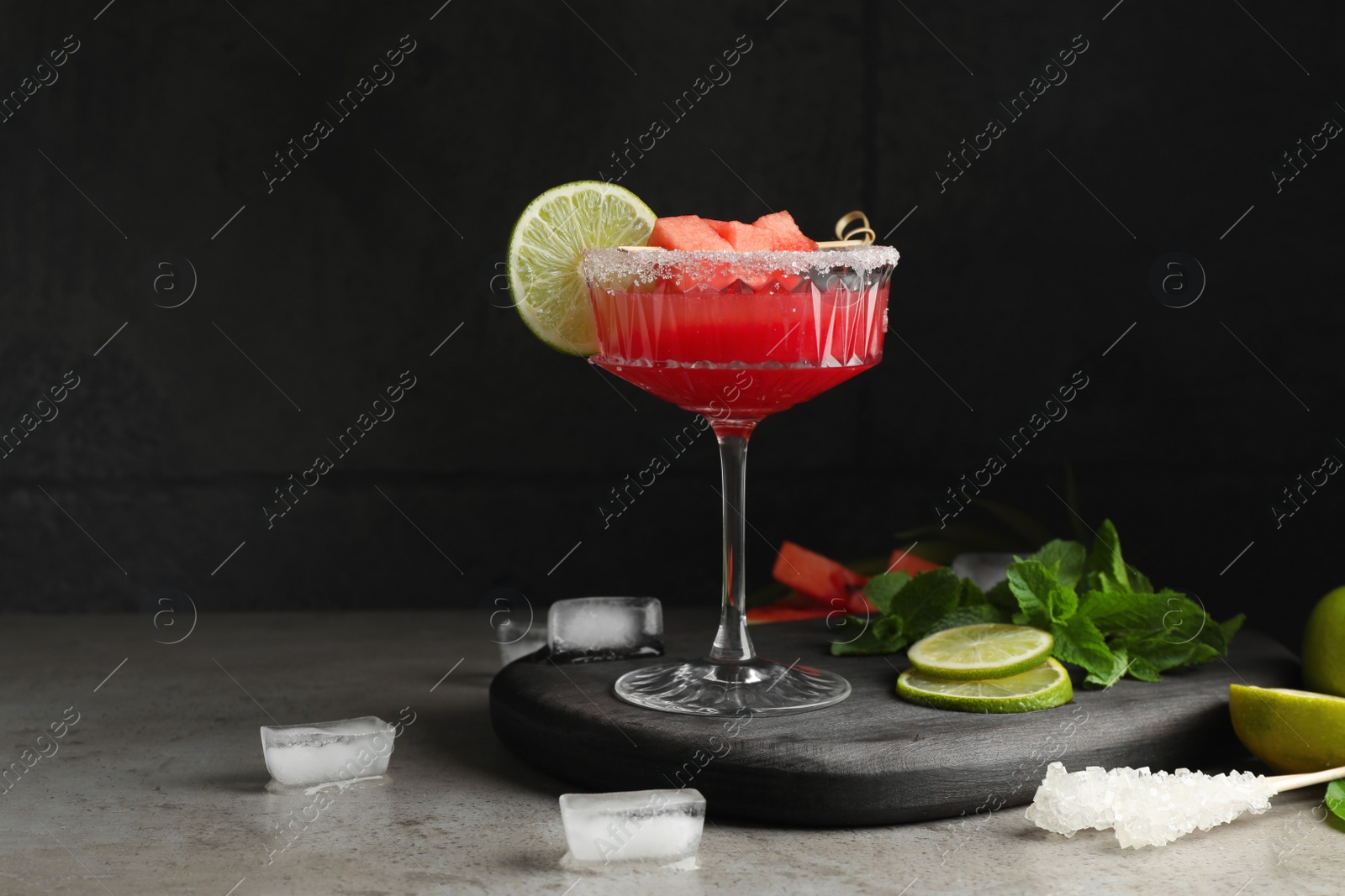 Photo of Cocktail glass of delicious fresh watermelon juice, lime, mint and ice on grey table