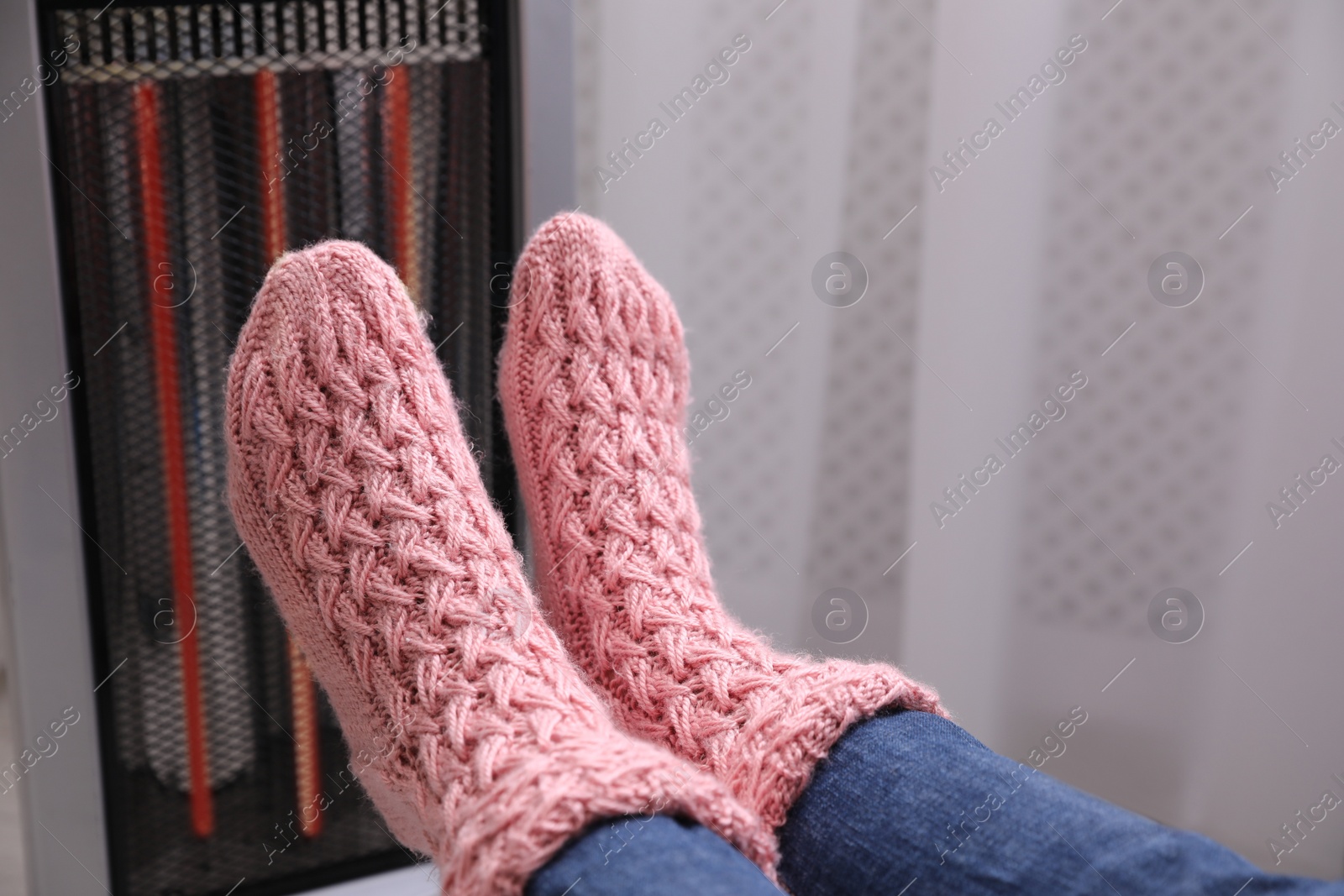 Photo of Woman warming feet near heater indoors, closeup