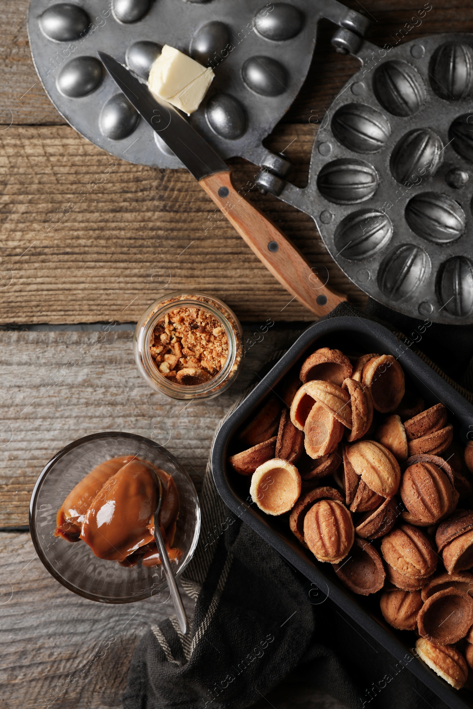 Photo of Making walnut shaped cookies. Cooked dough, mold, boiled condensed milk and nuts on wooden table, flat lay