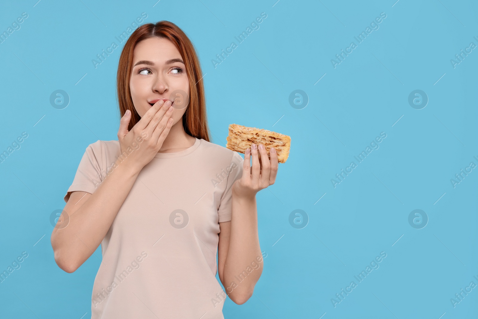 Photo of Emotional young woman with tasty cake on light blue background, space for text