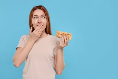 Photo of Emotional young woman with tasty cake on light blue background, space for text