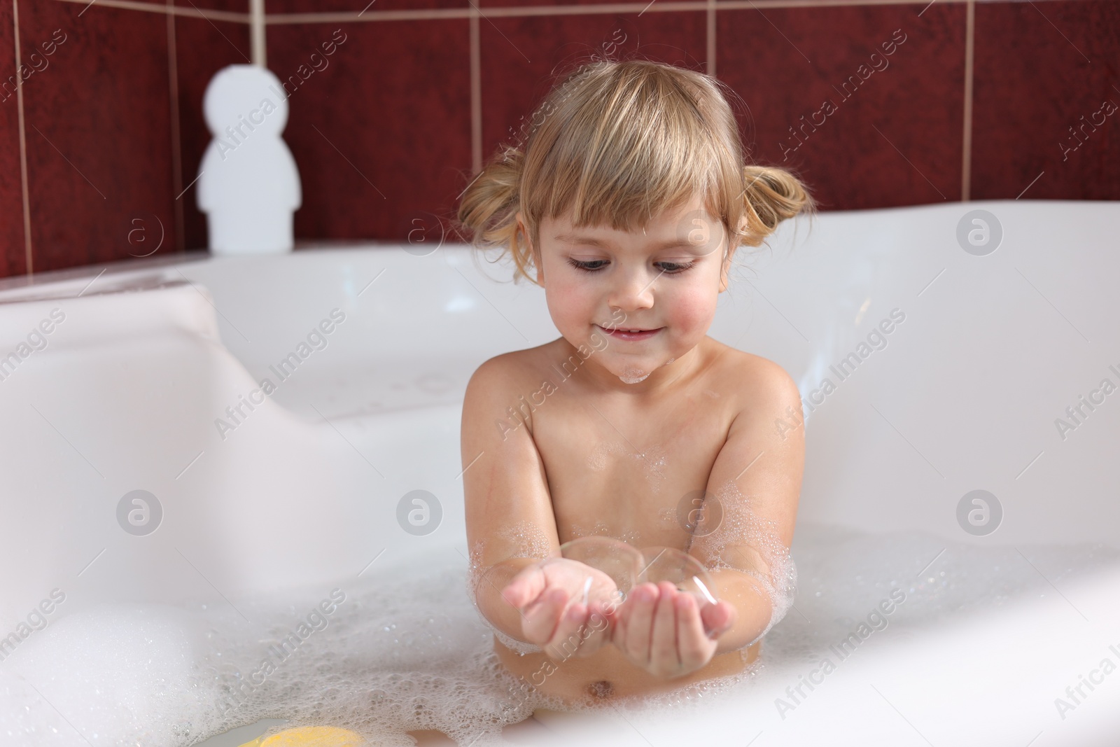 Photo of Little girl having fun in bathtub at home