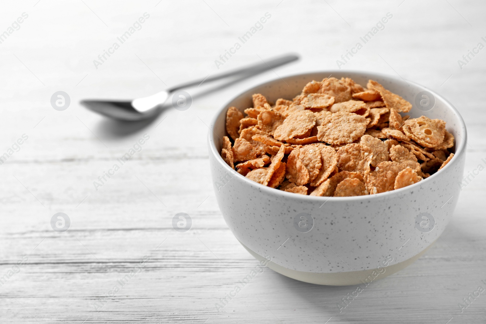 Photo of Bowl with cornflakes on light table. Whole grain cereal for breakfast