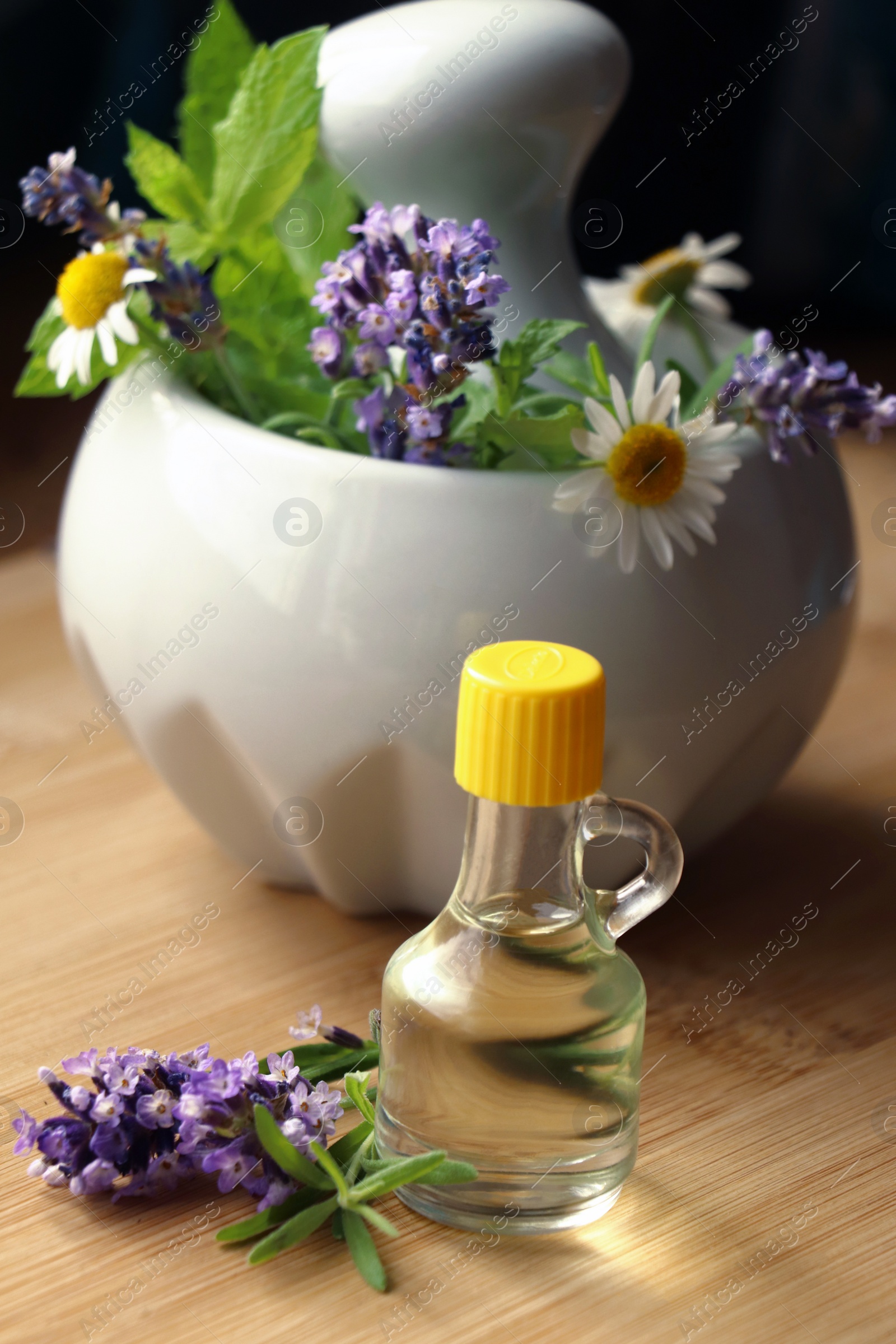 Photo of Bottle of natural lavender essential oil near mortar with flowers on wooden table