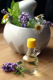 Bottle of natural lavender essential oil near mortar with flowers on wooden table