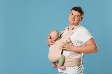 Photo of Father holding his child in sling (baby carrier) on light blue background. Space for text