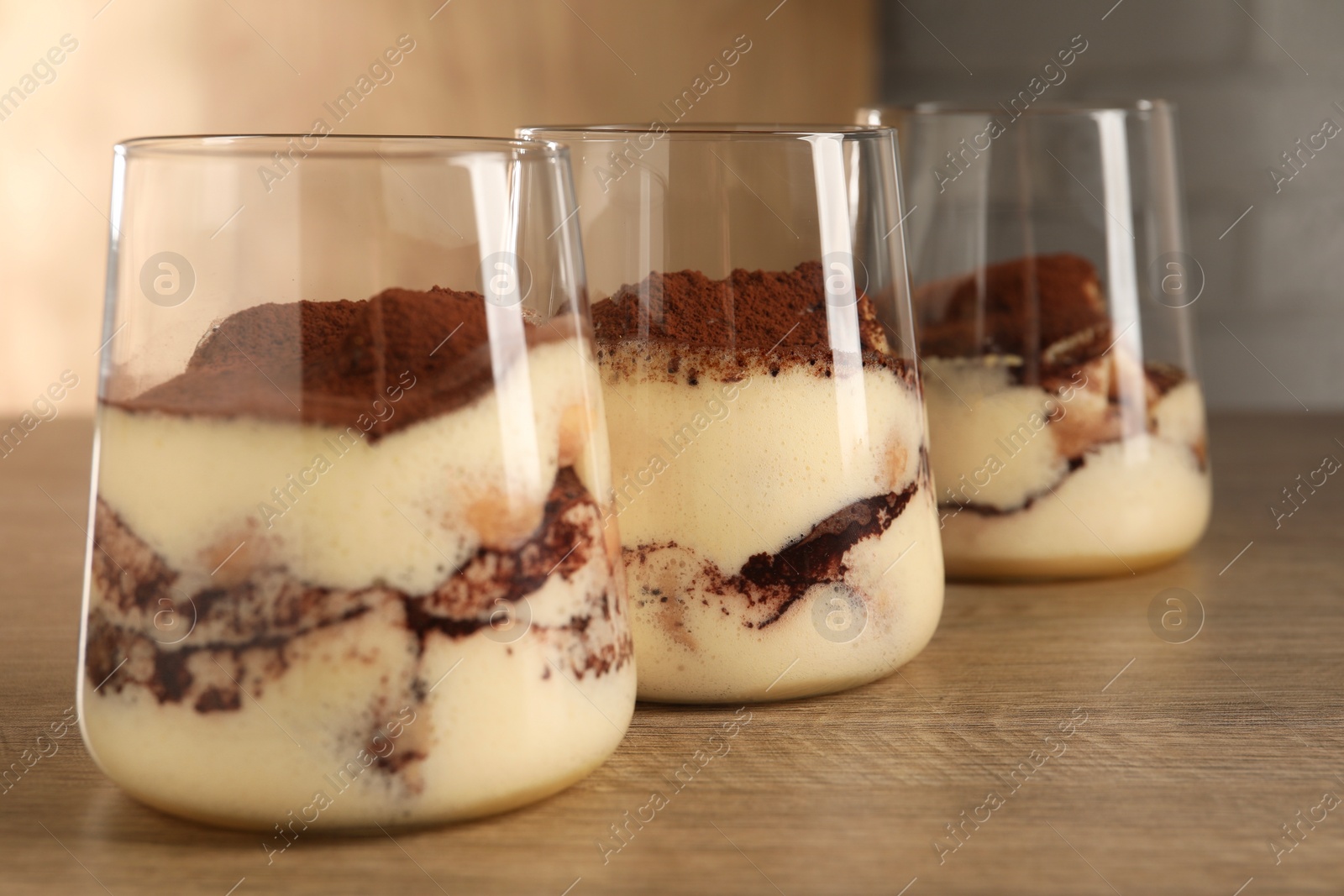 Photo of Delicious tiramisu in glasses on wooden table, closeup