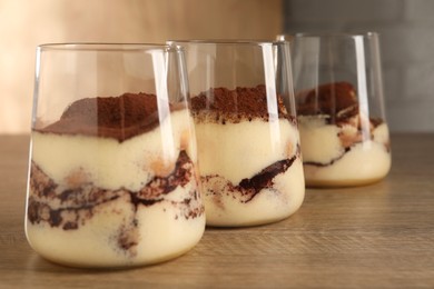 Photo of Delicious tiramisu in glasses on wooden table, closeup