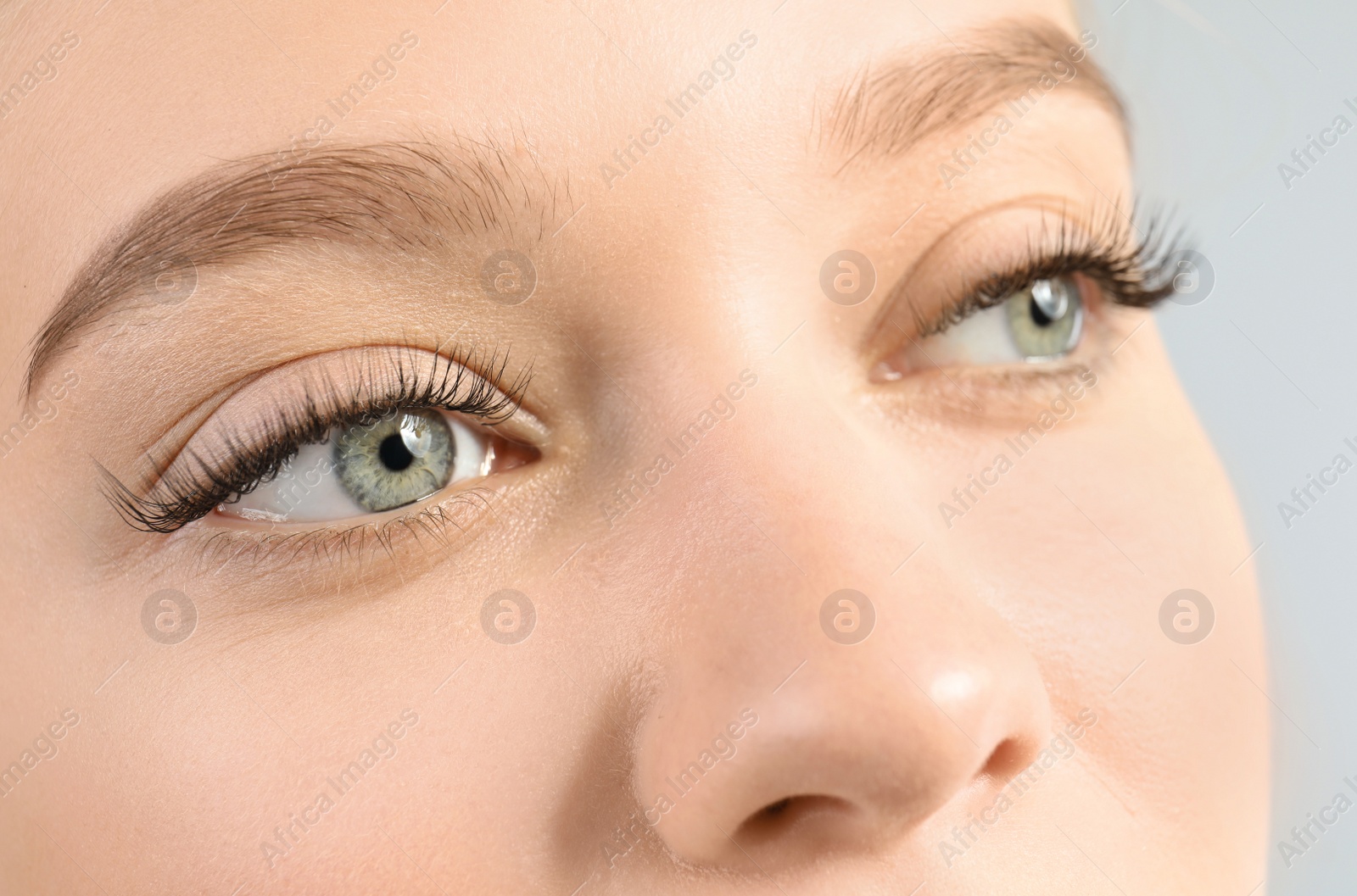 Photo of Young woman with beautiful long eyelashes on gray background, closeup. Extension procedure