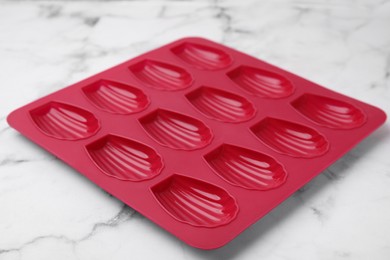 Red baking mold for madeleine cookies on white marble table, closeup