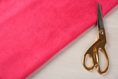 Photo of Scissors and pink fabric on light beige wooden table. Space for text