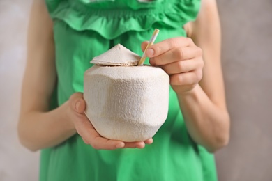 Woman with fresh coconut drink in nut on grey background, closeup