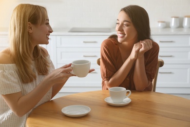 Photo of Young women talking while drinking tea at table in kitchen