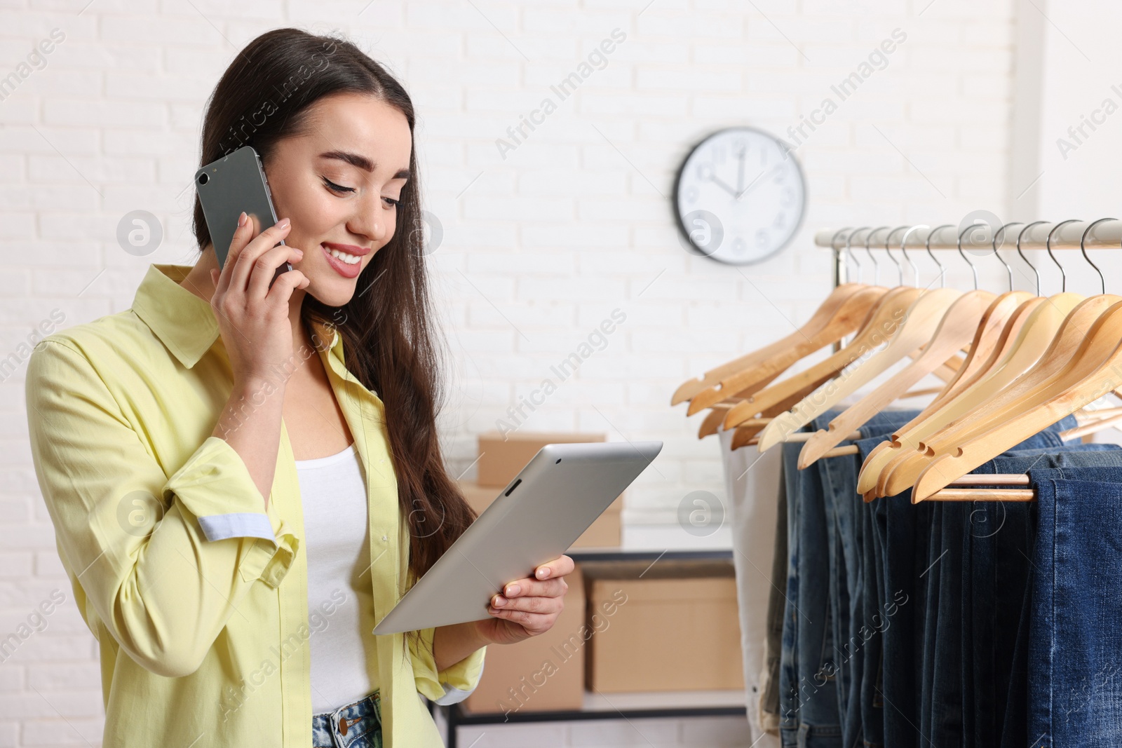Photo of Clothes seller with tablet talking on phone at workplace. Online store