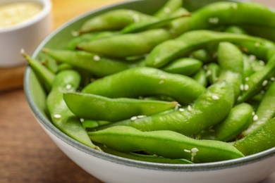 Photo of Bowl with green edamame beans in pods on wooden table, closeup