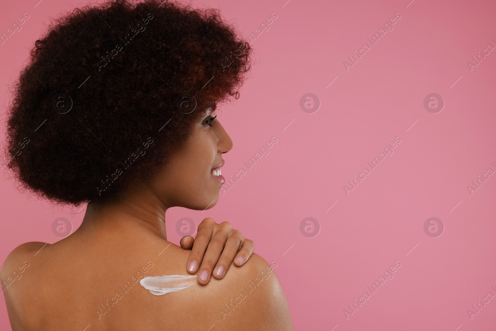 Photo of Beautiful young woman applying body cream onto back on pink background, space for text