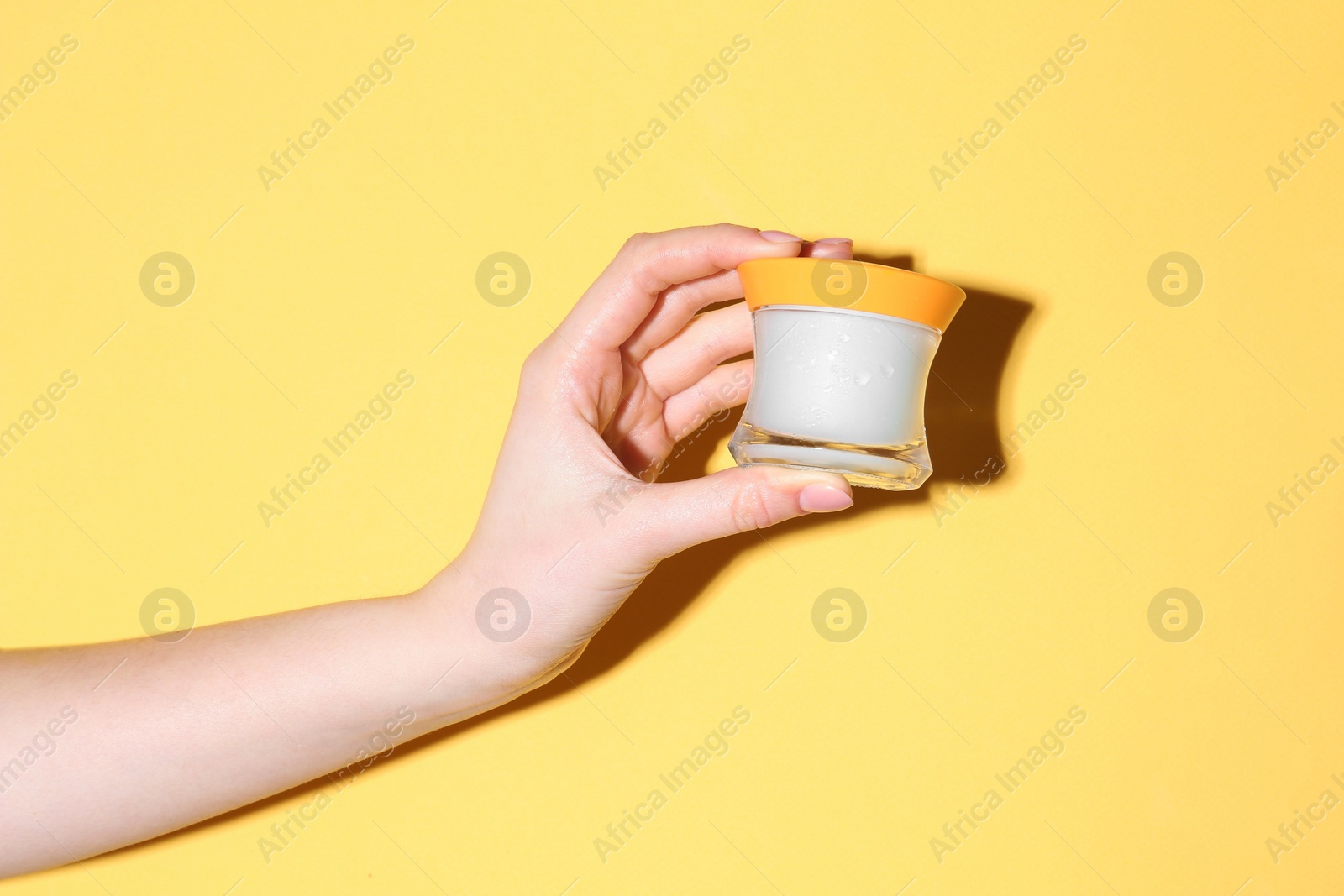 Photo of Woman holding jar of cream on yellow background, closeup