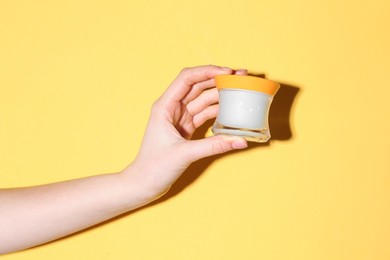 Photo of Woman holding jar of cream on yellow background, closeup