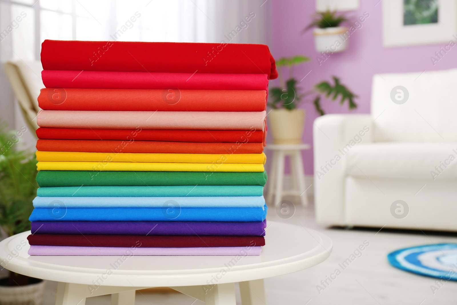 Photo of Pile of colorful t-shirts on table in living room