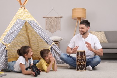 Photo of Father and children playing near toy wigwam at home