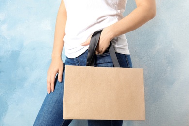 Woman holding mock-up of paper shopping bag on color background