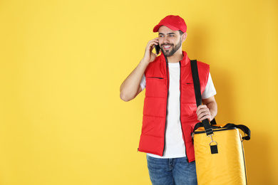 Photo of Courier with thermo bag and mobile phone on yellow background, space for text. Food delivery service