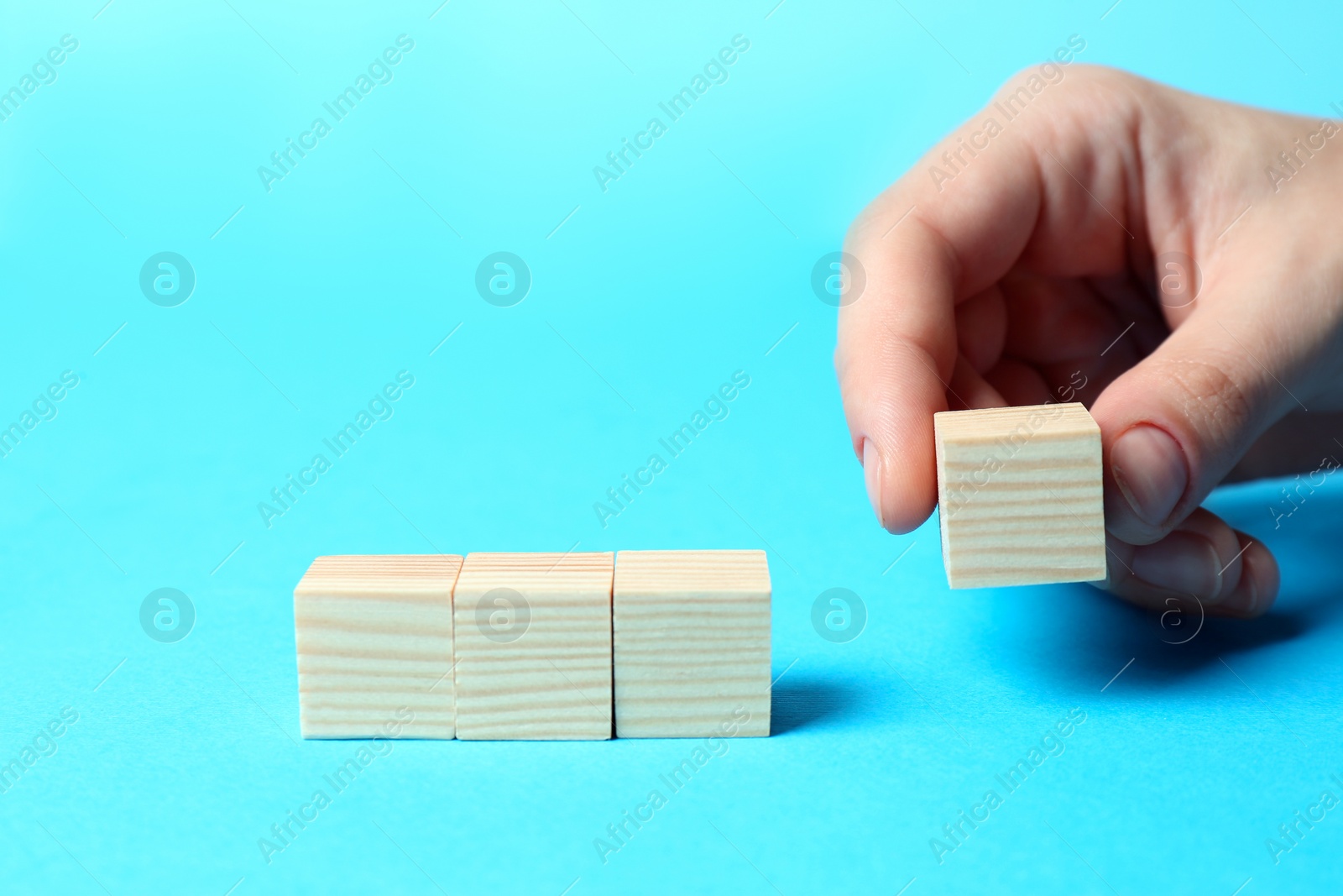 Photo of Woman arranging cubes on light blue background, closeup with space for text. Idea concept