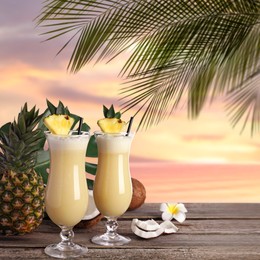 Image of Tasty Pina Colada cocktail on wooden table near ocean at sunset