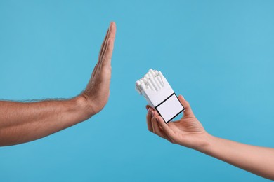 Photo of Stop smoking concept. Man refusing cigarettes on light blue background, closeup