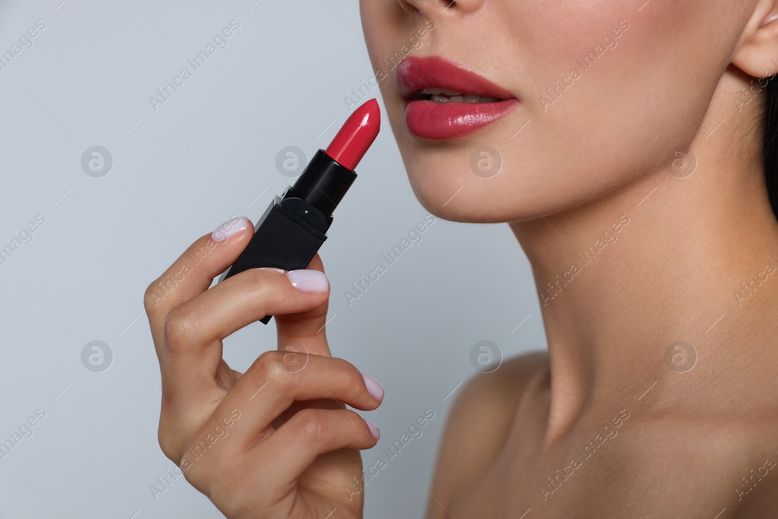 Photo of Young woman with beautiful makeup holding glossy lipstick on light gray background, closeup