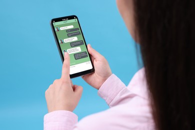 Woman texting with friend using messaging application on smartphone against light blue background, closeup