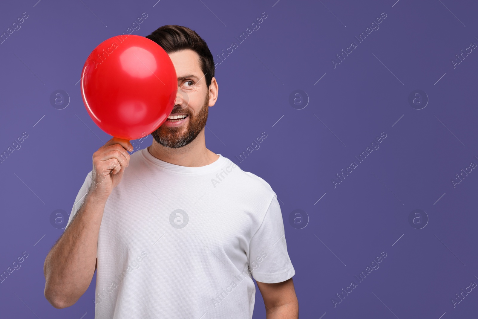 Photo of Happy man with red balloon on purple background. Space for text