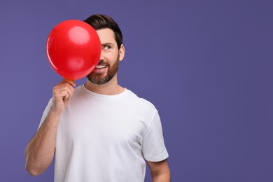 Photo of Happy man with red balloon on purple background. Space for text
