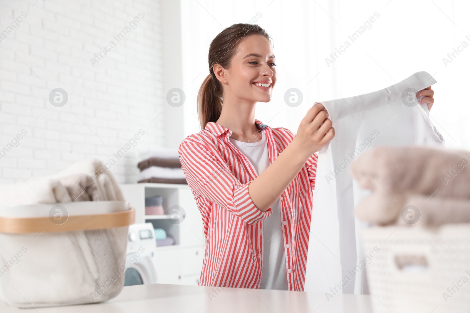 Photo of Happy young woman with clean shirt indoors. Laundry day